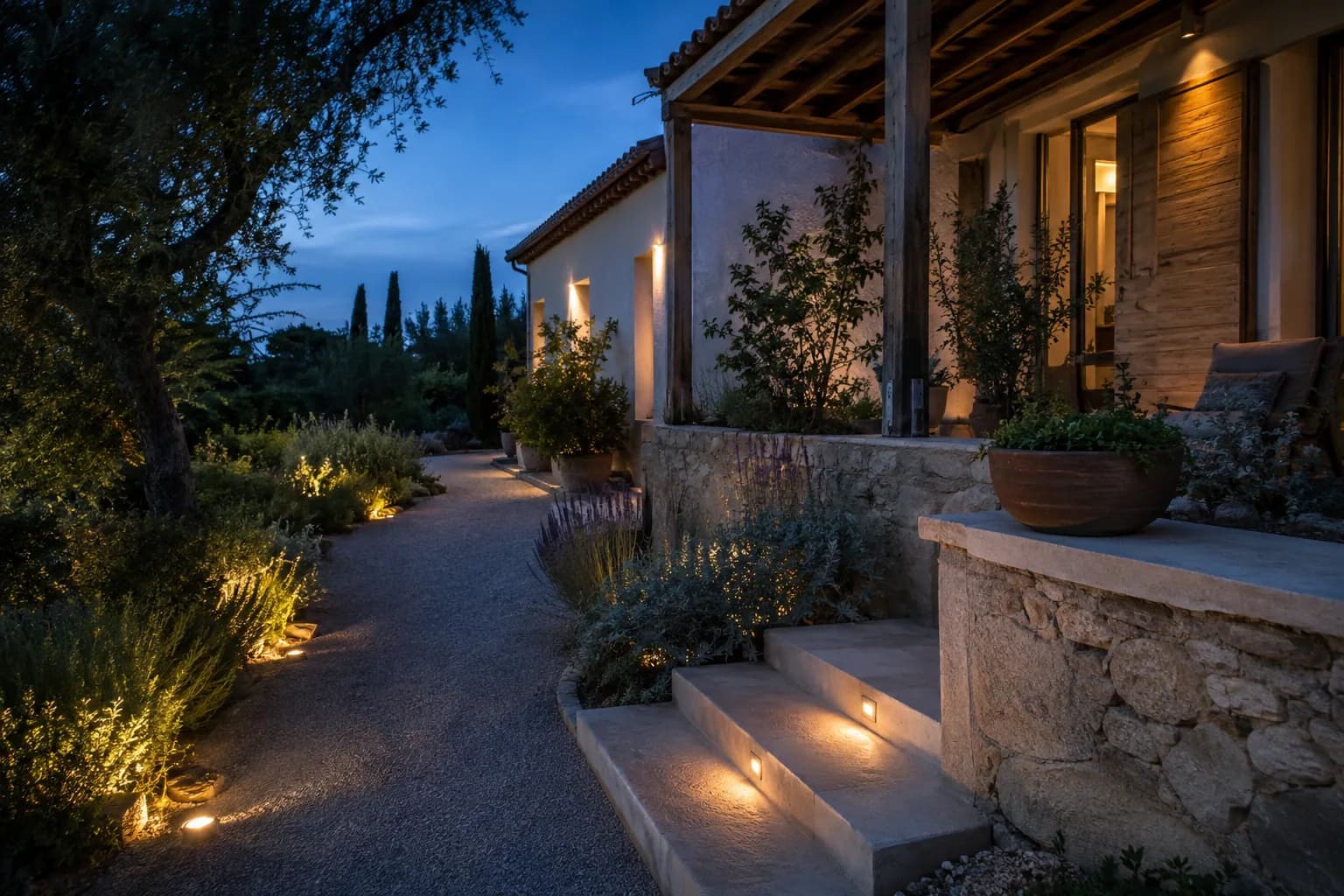 Terrasse et cheminement d’une villa méditerranéenne éclairés avec sobriété au crépuscule